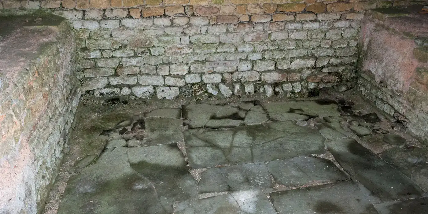 The excavated stone basin of the cold plunge room in the north wing of Chedworth Roman Villa, its walls lined with pale mortared blocks and its floor with flat slabs.