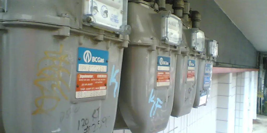 A row of old electricity meters bolted to an exterior wall, their dials and spinning discs visible behind grimy glass covers.