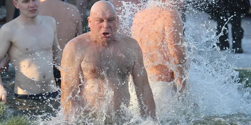 Three men wade chest-deep into open winter water, throwing up spray as they push forward, their faces tight against the cold.