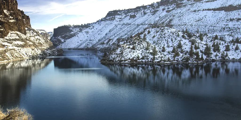 Still dark water running between snow-dusted basalt canyon walls at Lake Billy Chinook, Oregon, in winter.